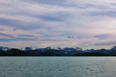 On the shore of the lake there are hills with tropical vegetation. Wraps of fog lie on the peaks,...