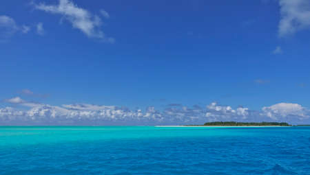 Idyll and paradise in the Maldives. Turquoise and aquamarine ocean hues. Picturesque clouds in the azure sky. In the distance is an island with a sandy beach and tropical vegetation. Endless summerの写真素材