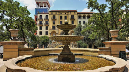 Fountain in the city square. Water splashes down the stone bowls. Round pool. Nearby are green trees, a residential building. South Africa. Johannesburgの写真素材