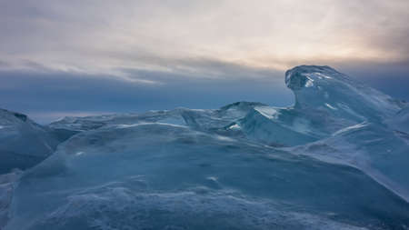 Ice hummocks against the sunset sky. Thick layers of transparent turquoise ice of bizarre shape. Lake Baikal. Russiaの写真素材
