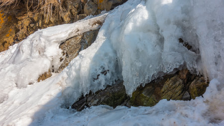 Ice splashes and snow on the rocks. Icicles begin to melt under the rays of the spring sun. End of winter.の写真素材
