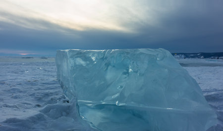 Ice shard on a snow-covered lake, close-up. Turquoise transparent shiny hummock against the sunset sky. Lake Baikal. Russiaの写真素材