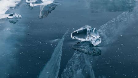 A transparent piece of ice of a bizarre shape lies on the thick blue ice with cracks. Mirror reflection. Lake baikalの写真素材