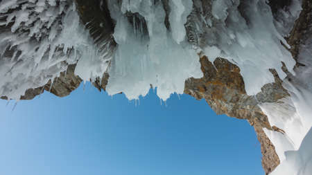 The ceiling of the stone grotto is covered with bizarre icicles that look like stalactites. Close-up against the blue sky.の写真素材