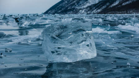 Ice shard close-up. A pale blue transparent shining crystal on the surface of a frozen lake. Reflection. Soft background with many small pieces of ice. Lake baikalの写真素材