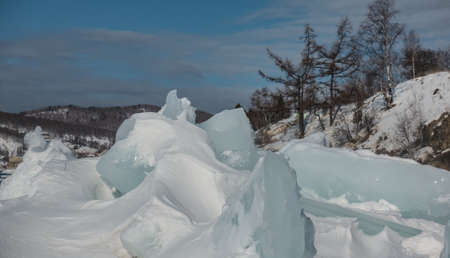 Bizarre ice hummocks, covered with snow on a frozen lake. The background is mountains, bare...