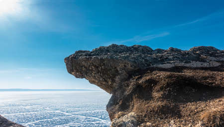 A flat rock overhang a frozen lake against a blue sky. Stone texture. Cracks and snow patterns on the ice. Winter day. Baikalの写真素材