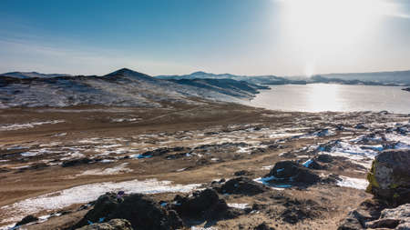 The frozen lake is surrounded by mountains. Snow covered earth. Sun glare on ice. There are no...