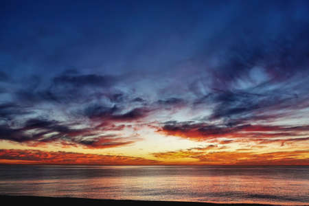 Dramatic sunset over the sea. Dusk. There are purple and scarlet clouds in the blue sky. Orange glow over the horizon. Reflection on the surface of the water. Black seaの写真素材