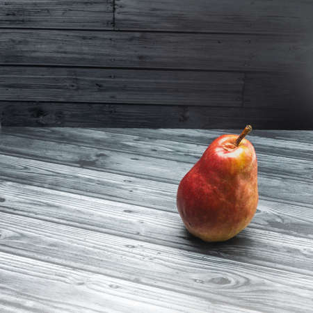 A ripe red pear with a shiny skin lies on gray planks. Close-up. Side view. Bottom right cornerの写真素材