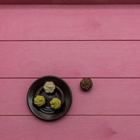 On a brown saucer are chocolates with cream and pistachio filling. One candy nearby, on pink boards. Top view. Left bottom corner. Copy spaceの写真素材