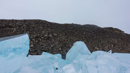 A block of blue ice hummocks against the background of a granite rock devoid of vegetation. Shiny...