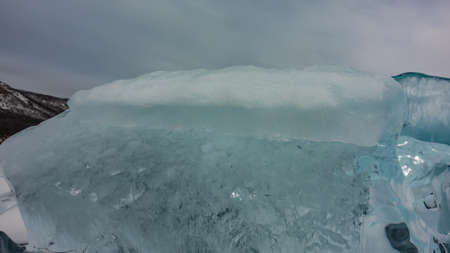 Turquoise ice hummock against the background of the cloudy sky. Close-up. Texture. Details. Glare of...