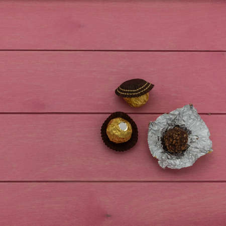 Chocolate candies wrapped in a golden foil lie on a pink wooden table. One candy deployed. Top view. Close-upの写真素材
