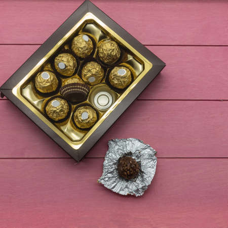 The brown cardboard box is filled with chocolate candies, wrapped in a golden foil. One candy...