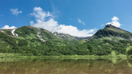 A mountain range on the shore of a calm transparent lake. There is green vegetation on the slopes,...