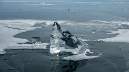 A shiny transparent piece of ice on a frozen lake. The bizarre shape, the glare of the sun on the...