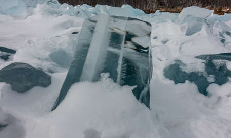 A transparent turquoise ice floe on a frozen lake is surrounded by snow. Glare and reflection on the...