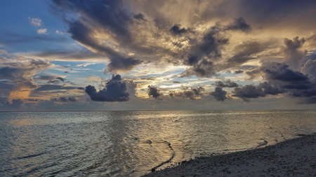 Golden sunset in the Maldives. The sun highlights the clouds in the blue sky. The calm surface of...
