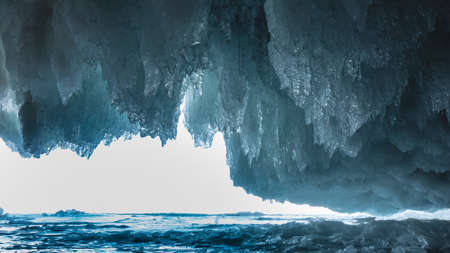 The exit from the ice cave is surrounded by rows of blue shiny icicles, like lace frills. Bright light ahead, the surface of a frozen lake. Baikalの写真素材