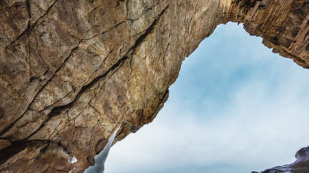 A triangular passage in a granite rock. Close-up. The texture of the stone. Cracks and layers are visible. Bright blue sky and light clouds are ahead. Baikal.の写真素材
