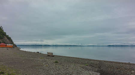 Pacific Ocean coast. Cloudy. There is a lonely wooden bench on the pebble beach. Cumulus clouds are above the horizon. Reflection on the smooth surface of the water. Petropavlovsk-Kamchatskyの写真素材
