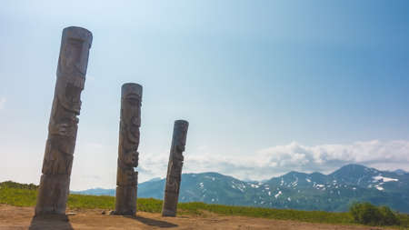 Old ritual pillars against the blue sky. Wood carving. In the distance is a mountain range with...