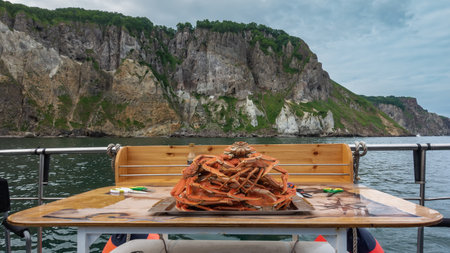 On the yacht, on the table, there is a tray. Boiled snow crabs are stacked in a slide. Legs and claws are visible. The background is the ocean, the rocky coast of Kamchatkaの写真素材