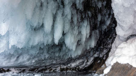 Rows of thick shiny icicles hang from the roof of the cave. Fancy shape. Close-up. Baikal.