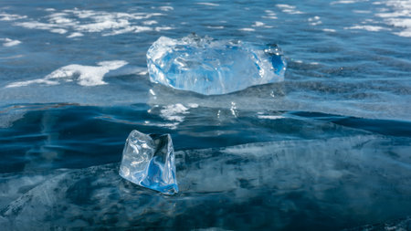 Shiny shards of ice lie on the smooth blue surface of the frozen lake. Cracks extending into the depths are visible. Close-up. Details. Baikalの写真素材