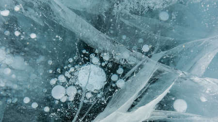 Transparent turquoise ice. Close-up. Full screen. Details. Intersecting cracks, bubbles of frozen...