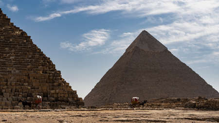 Two great pyramids - Cheops and Chephren on a background of blue sky and clouds. Horse-drawn carts...