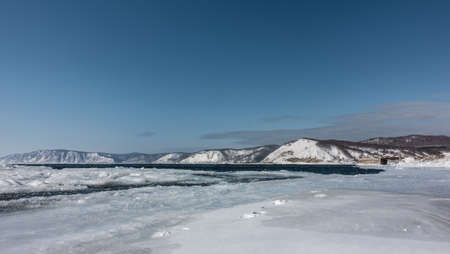 The blue ice-free river Angara in winter. Footprints on the icy shore. A snow-covered mountain range against an azure sky. Siberiaの写真素材