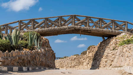 The decorative bridge in the park is made of palm trunks. Lattice railings against a bright blue sky. Under the bridge, between the stone walls, there is a path. Alexandria. Egyptの写真素材