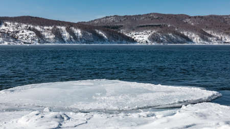 Blue ice-free river in winter. Ripples on the water. Ice floes near the shore. Snow-covered and...