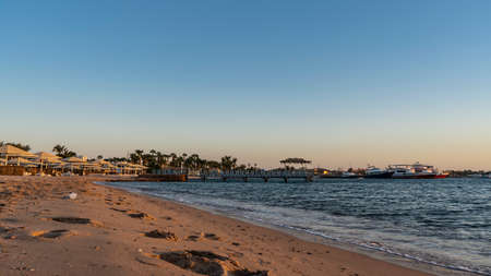 A beach on the Red Sea coast. Footprints in the sand. Umbrellas from the sun and loungers are in a row. Above the blue water there is a path, a canopy. Boats are visible in the distance. Egyptの写真素材