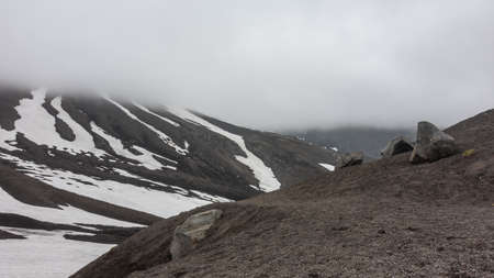 Boulders lie on the rocky volcanic soil. There are areas of melted snow on the slopes of the...