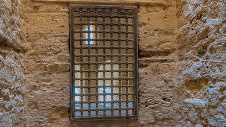 The interior rooms of the ancient Citadel of Qaitbay have rough stone walls. Through the barred...