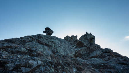 Granite rock against the blue sky. There are cracks and dry grass on the slopes. Several pyramids of stones are stacked on the top. Siberia.の写真素材