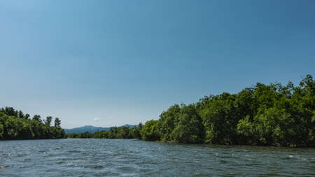 The blue River flows between banks overgrown with green vegetation. Ripples on the water. Mountains...