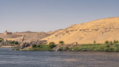 On the river bank there is a strip of green vegetation, boulders. High sand dunes against the sky....