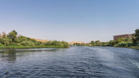 The river flows calmly. There is green vegetation on the banks. A tourist boat is sailing on blue...