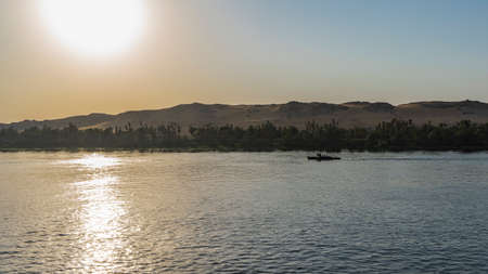 Evening in Egypt. The sun shining is low over a sand dune. The boat is sailing on a calm river. A sunny path on the water. clear sky. copyspace. Nile.の写真素材