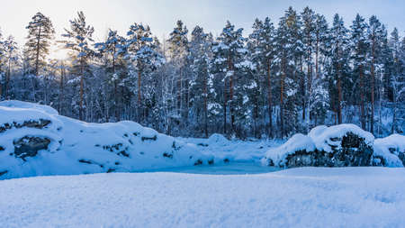 Pure fluffy snow covers the valley. There are picturesque snow-covered boulders on the bank of a...