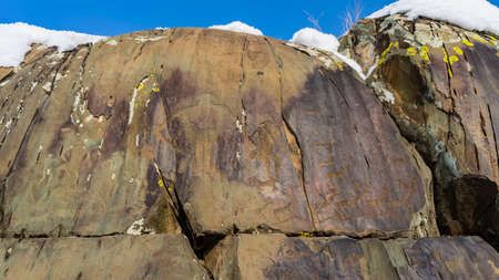 ancient rock art. Primitive drawings of people and animals are carved on huge weathered stones. blue sky. Altai. Kalbak Tashの写真素材