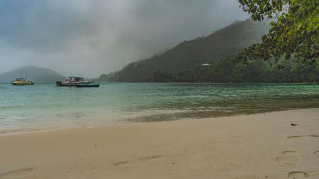 Rainy day on the beach. The sky is cloudy, the mountains are hidden in fog. There are boats on the...