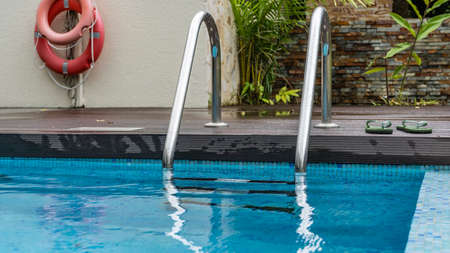 A fragment of a swimming pool. A metal staircase with a railing descends into the blue water....