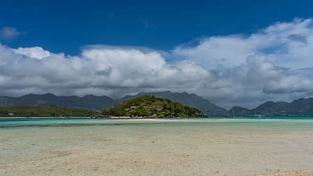 The island in the Indian Ocean is overgrown with tropical vegetation. Houses are visible through the...