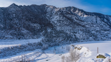A picturesque mountain against the blue sky. The frozen river winds through a valley covered with pure untouched white snow. Frosted trees on the banks. towers of power linesの写真素材