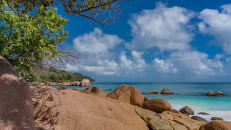 Piles of picturesque granite boulders on the shore of the turquoise ocean. A green hill in the...